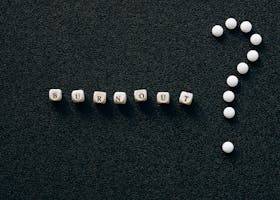 A visual representation of burnout and questioning with beads forming words and symbols on a textured black surface.